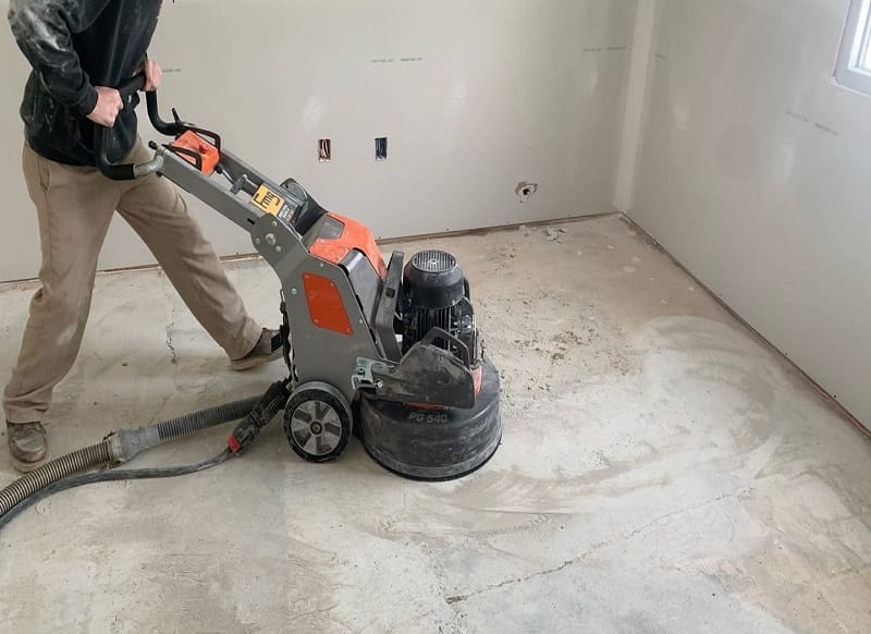 Industrial floor undergoing grinding with sparks flying, revealing a clean concrete surface beneath.