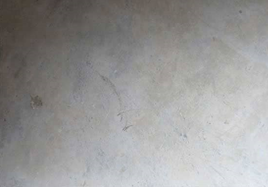 Close-up of a concrete floor undergoing scarification, showing a rotating head with grinding teeth removing the top layer.