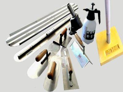 Close-up of various decorative concrete texture tools like stamps, stencils, and trowels on a shelf in a Pune, India hardware store.